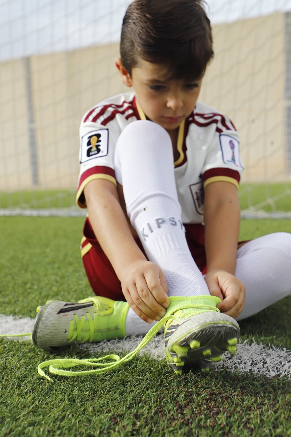 Niño atándose las botas sobre el césped junto a la línea del campo